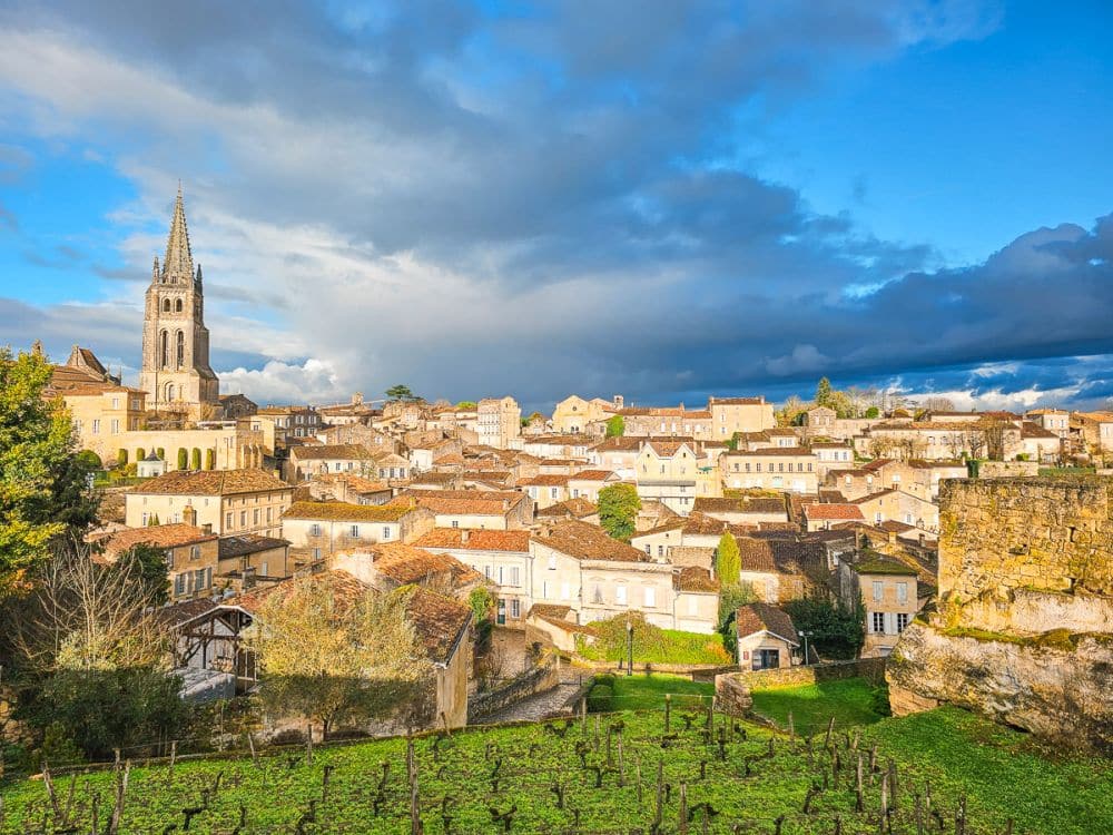 View over Saint Emilion with plastered houses with tile roofs and a church towering over them.