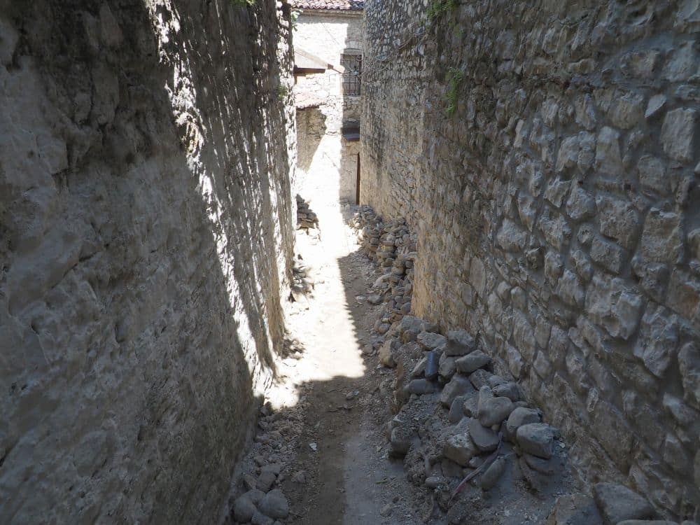 Very narrow, steep, and rocky path between stone buildings.