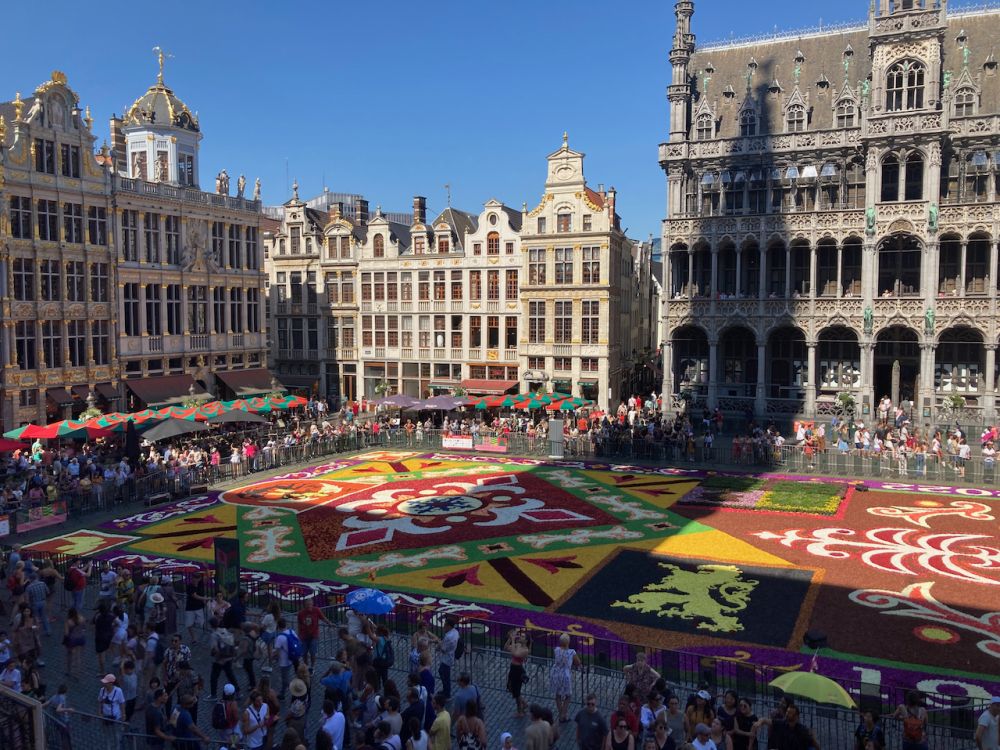 A portion of La Grand-Place with people around the edges and the center carpeted in brightly-colored flowers.