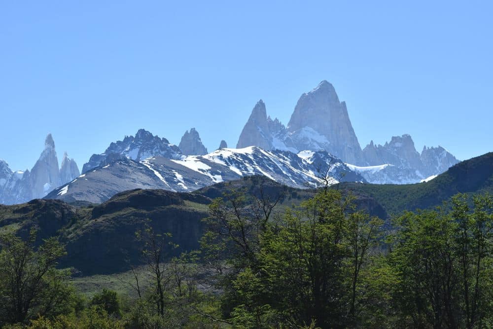 Green hills nearby, very jagged snow-covered mountains beyond them.