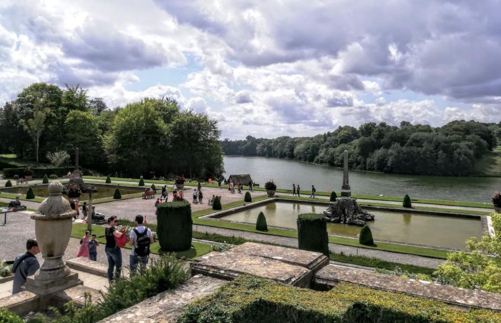 View of a formal garden and a lake and forest beyond that.