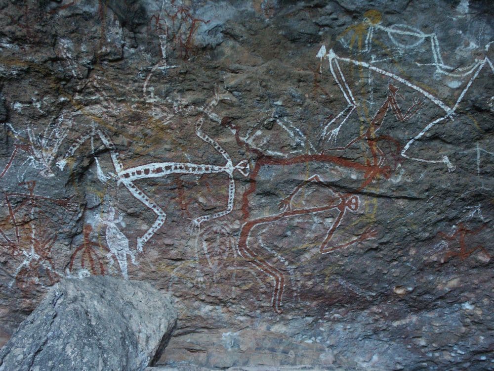 Drawings of humans in red and white on a rock face.