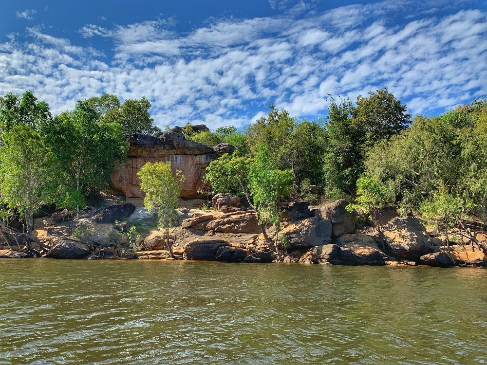 Seen across a river or lake, a tree-covered hill with a cliff face.