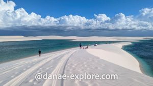 View along a dune, people in bathing suits, blue water in the pond below.