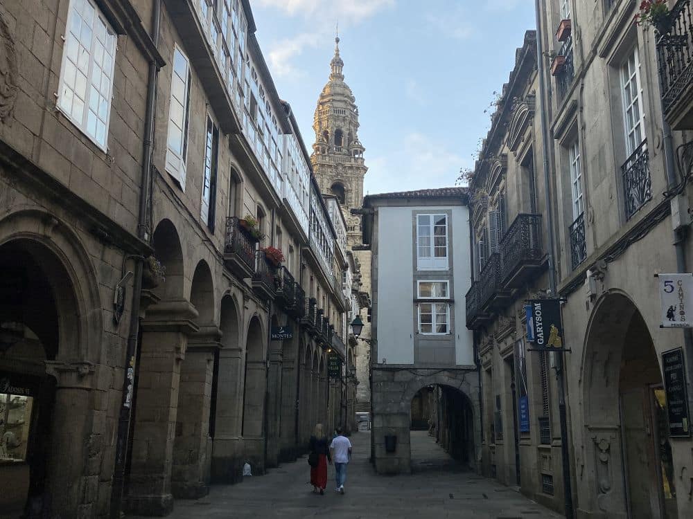 a narrow street with one of the cathedral towers in the background.