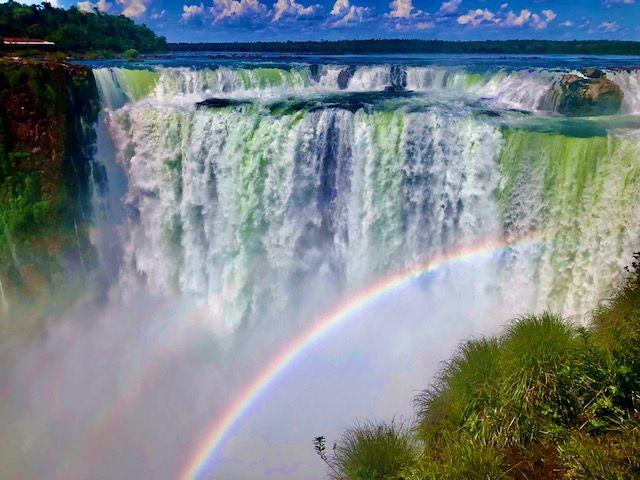 A high and wide waterfall with, in front of it, a rainbow.