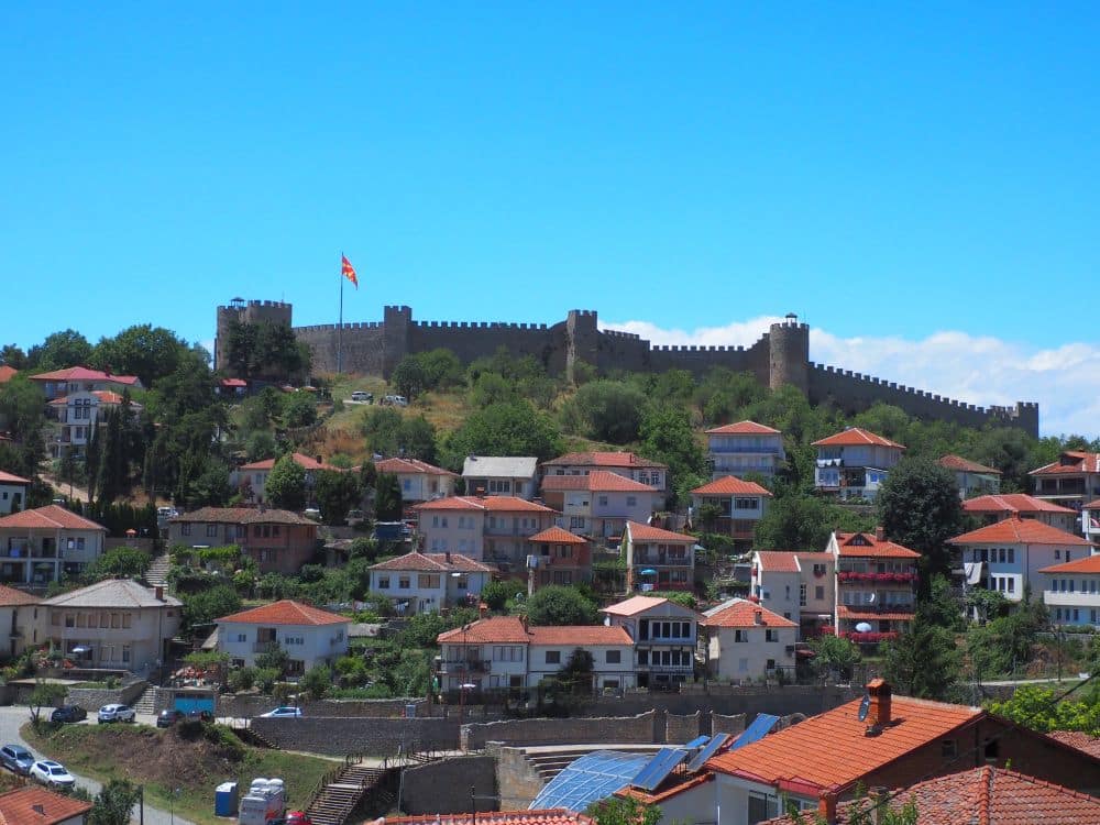 View of a hill covered with houses - at the top, a crenelated castle wall.