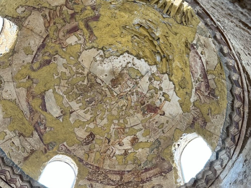 Looking up at a domed roof with remnants of images on it.