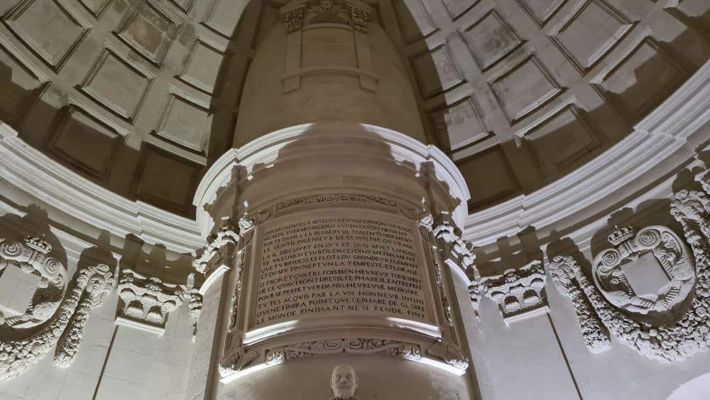 Looking up at a carved stone plaque, the edge of the ceiling with its classical carvings, and a piece of the domed roof, also carved.