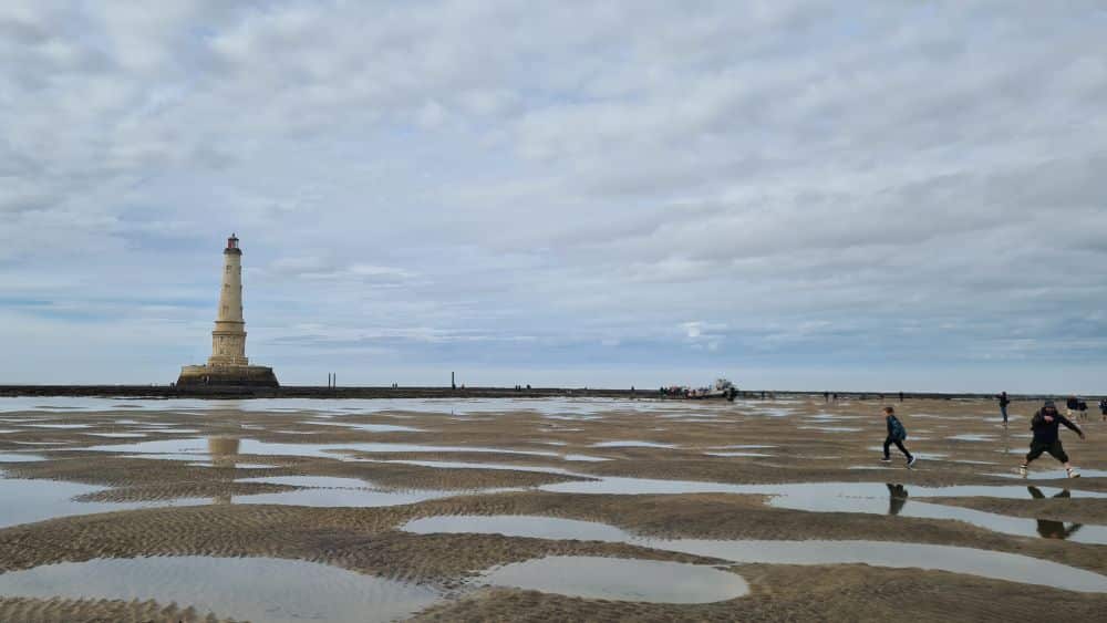 Sand with puddles of water, and the lighthouse in the distance.