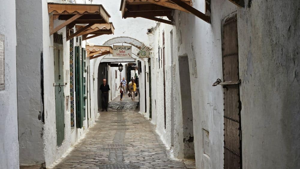 A narrow street lined whitewashed houses, whose eaves nearly meet in the middle.