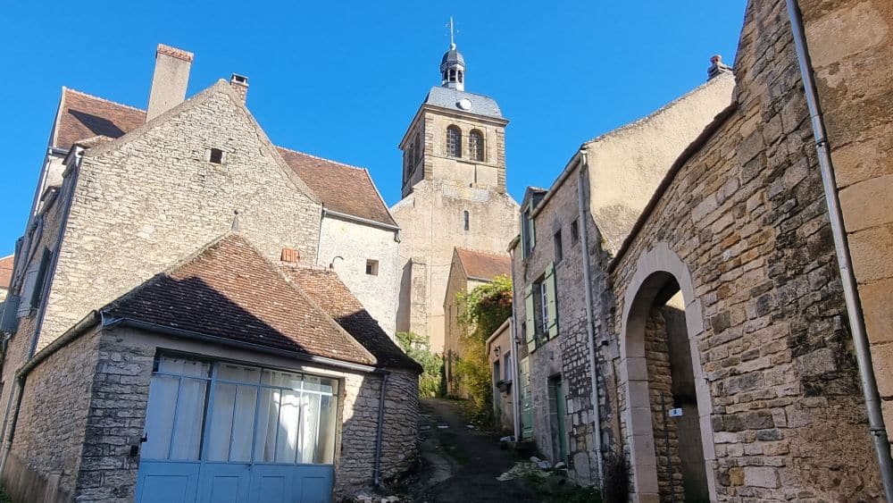 A narrow street of stone buildings slants uphill toward a church tower.