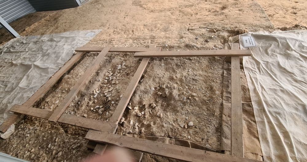 A section of the dirt floor is uncovered and shows a scattering of pieces of flint.