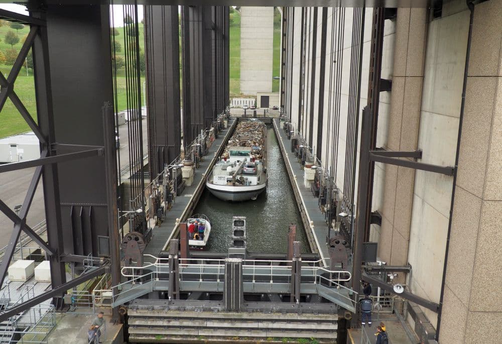 A long narrow tank of water with a long river cargo ship in it, along with a tiny pleasure boat.