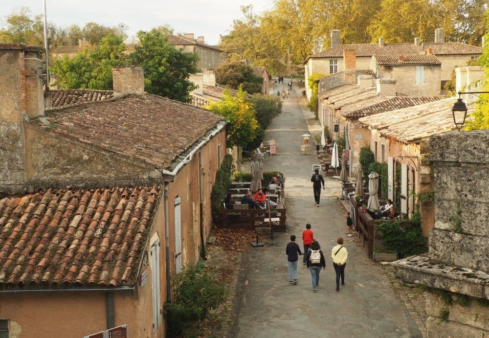 A view from slightly above along a street of small stone houses, people walking down the middle of the street.