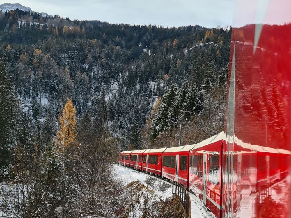 A red train curves to the left, a tree-covered mountain behind it.