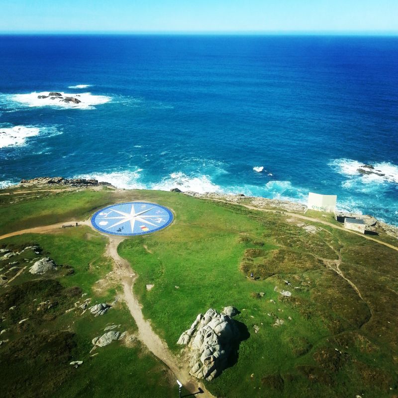 View from the lighthouse shows a path across a grassy area and a rocky coast with blue sea.