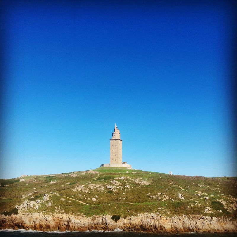 The lighthouse as seen from the water, standing on a hill.