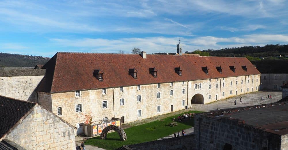 A large long building of white stone with a red roof.