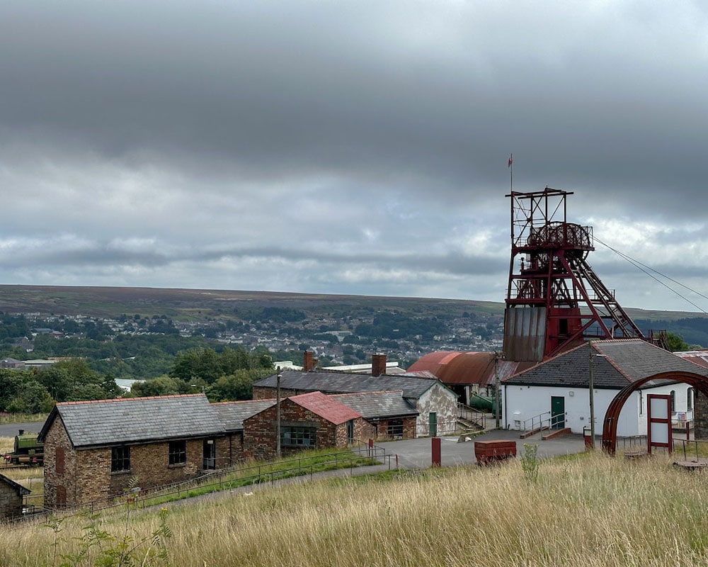 A cluster of small stone buildings with metal roofs and a tall structure of iron bars.