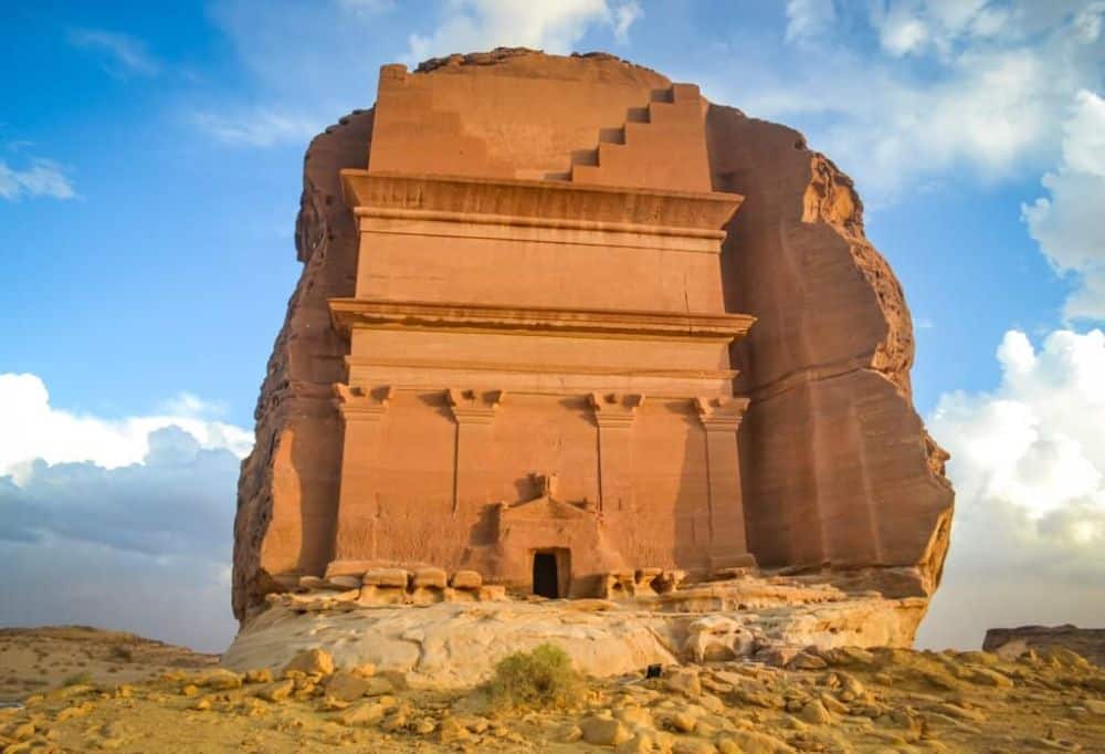 A huge rock emerging from the desert floor, and one side of it is carved into a grand entranceway.