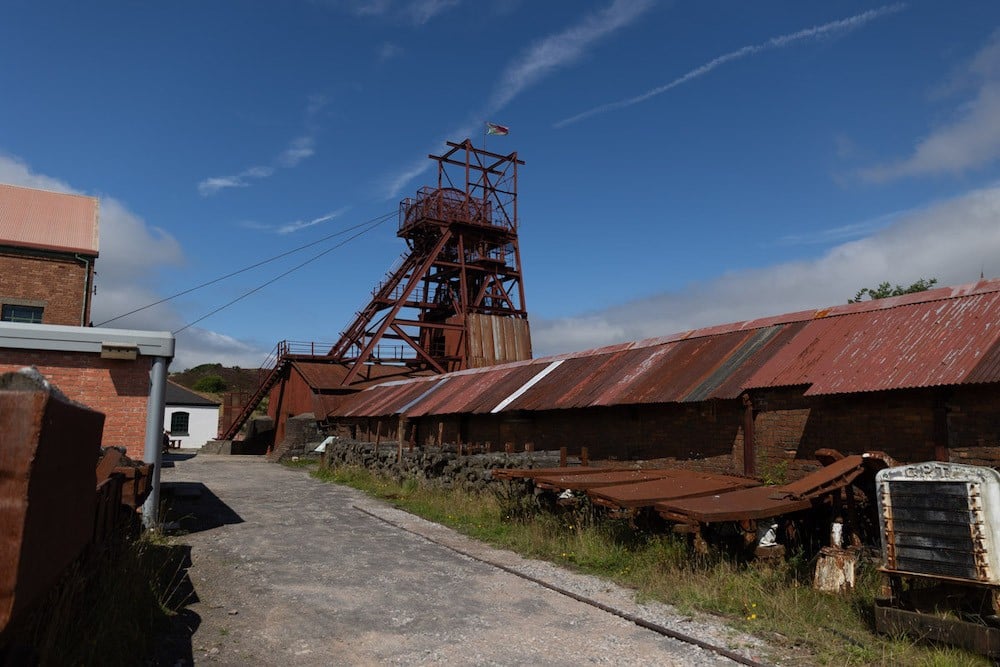 A long low shed with rusted metal roof and, beyond it, a tall structure.