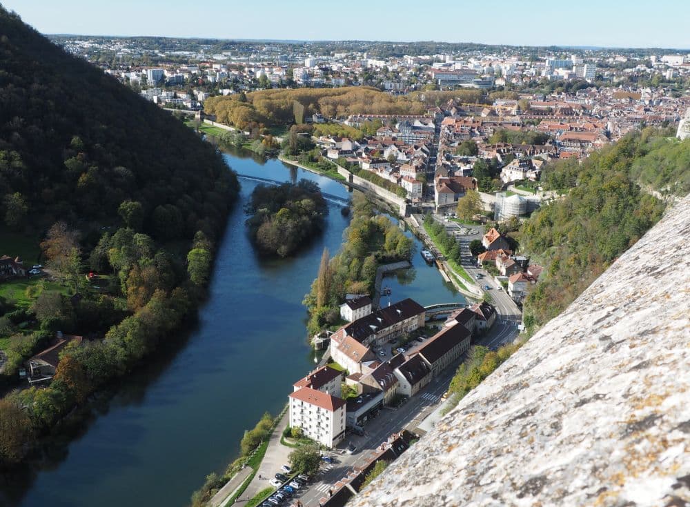 Far below is a view of a river winding between a steep hill and a city.