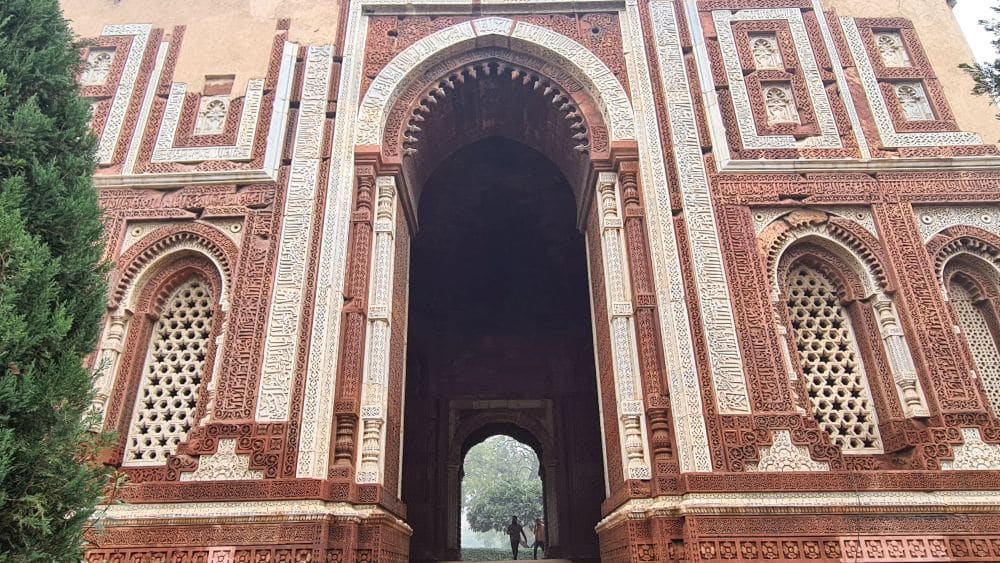 An archway in red and white stone, carved with calligraphy.