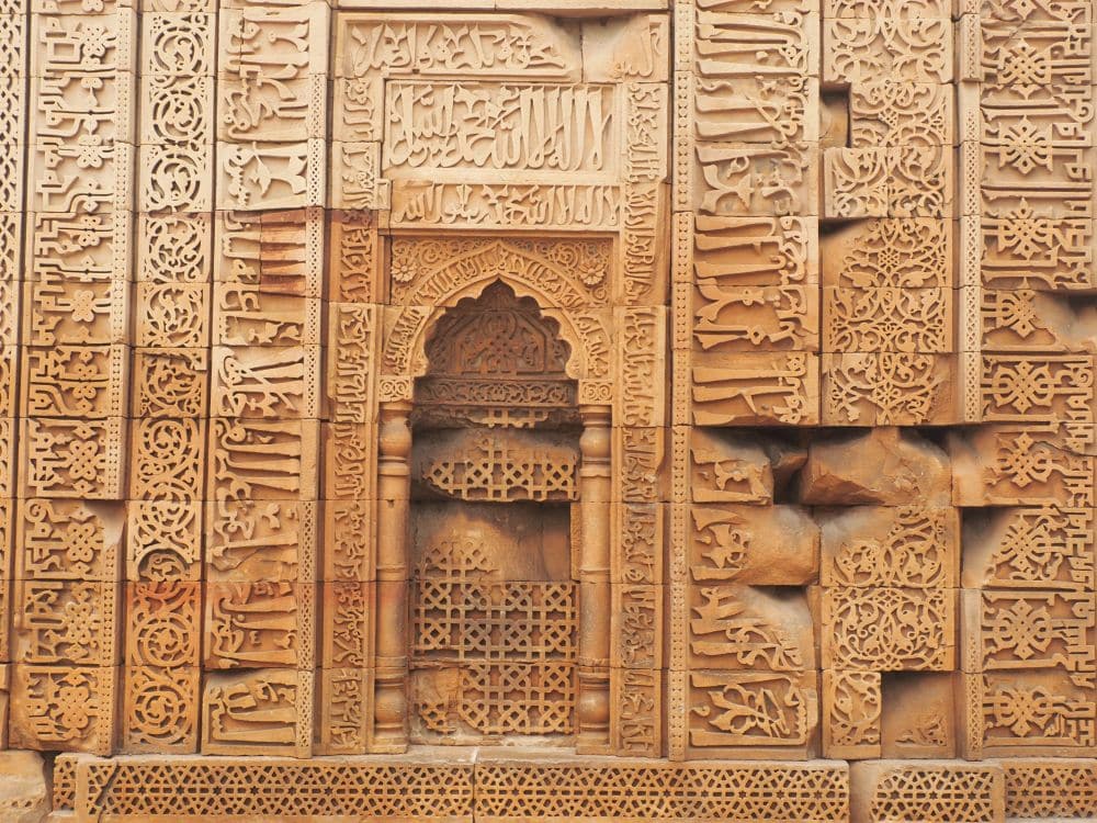 A very detailed wall carving, covered in calligraphy, with a niche in the middle.