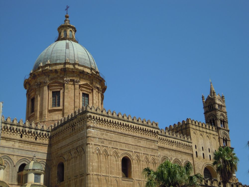 Looking up at the top of a building: crenelations around the edges and a rounded tower with a dome on top of it.