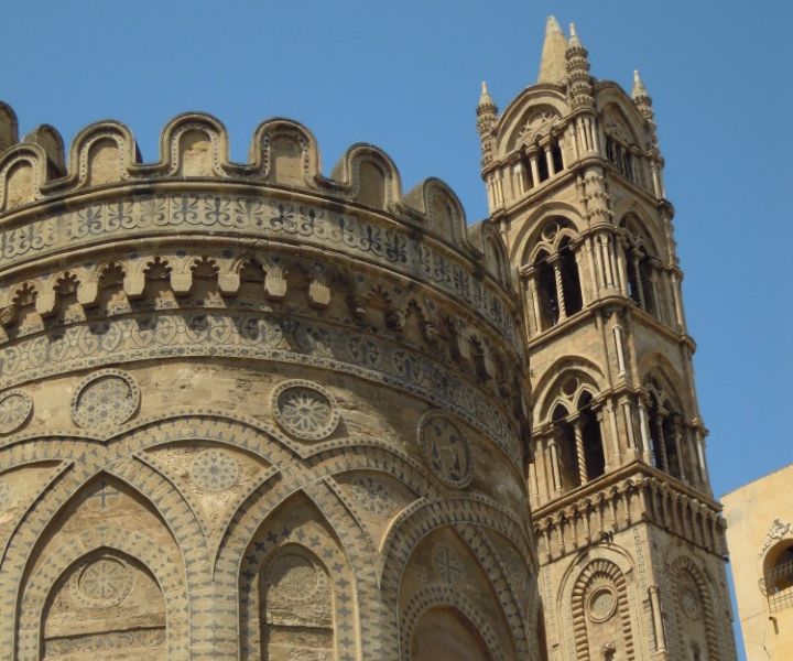 A segment of a rounded building with crenelations around its top and a square tower beside it.