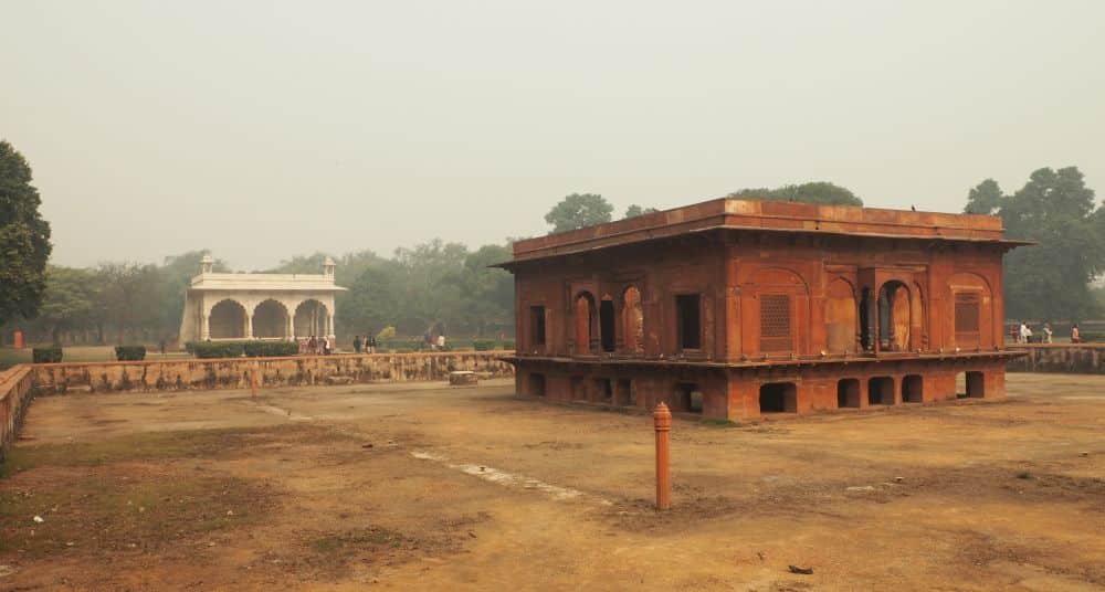 Nearby, a red stone, single-story square building. Beyond that, a pavilion with columns in white marble.