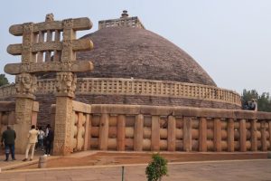 A hemispherical building with a brick roof and stone fence around it and an ornamental gateway.