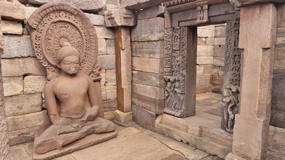 A sitting buddha statue on the left, a doorway with carvings around it on the right.