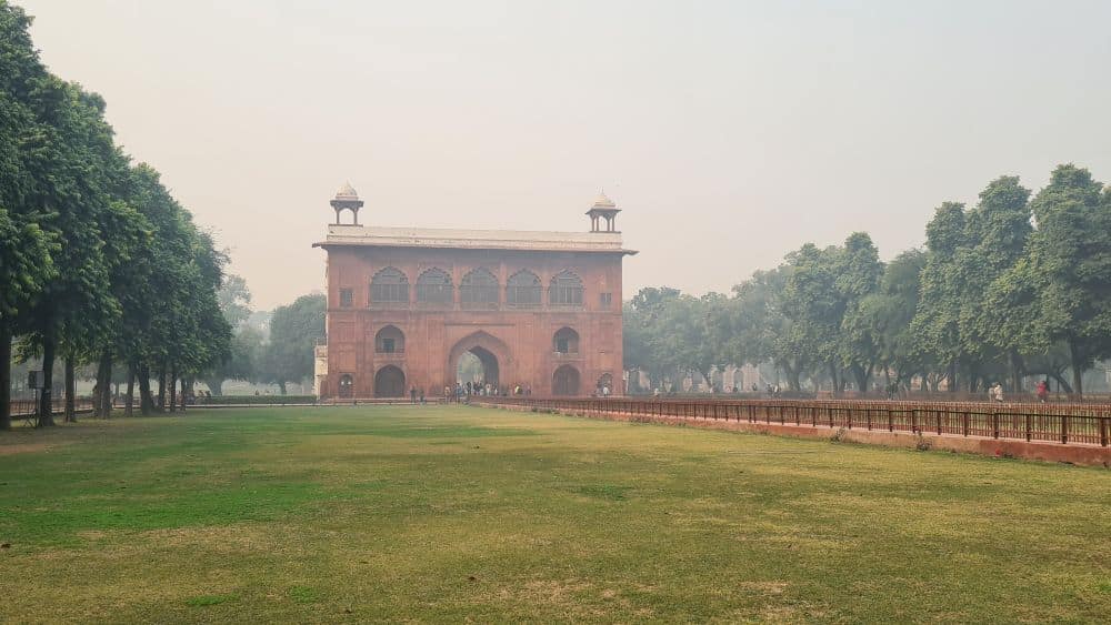 Across a grassy field, a large arched gateway in red stone.