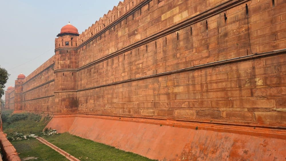 A long and high wall of reddish stone with crenelations along the top.