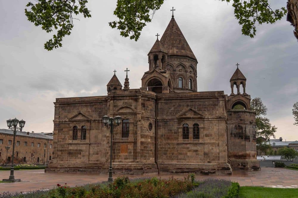 A rather square building with a round tower in the middle with a pointed roof.