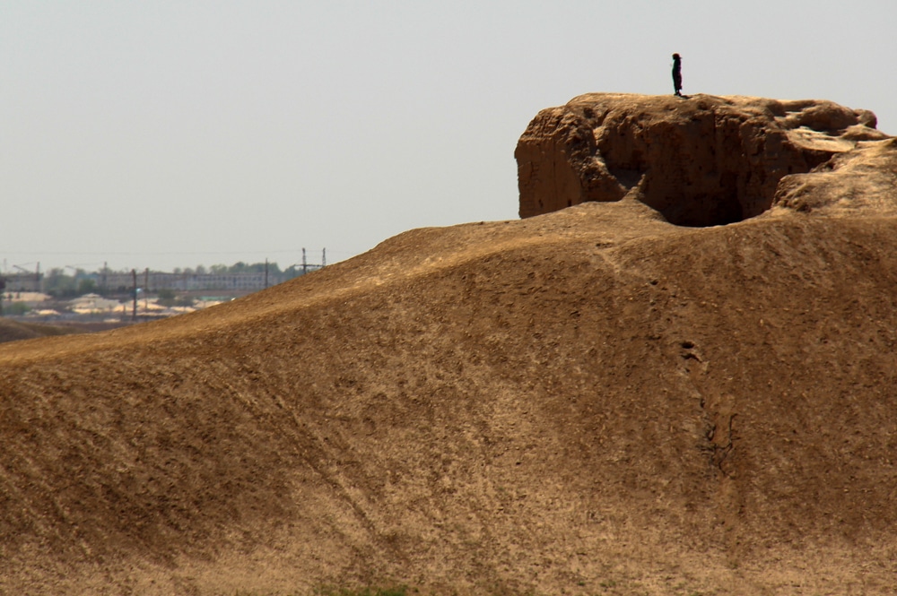 A woman stands on a high structure, perhaps the remains of a city wall.