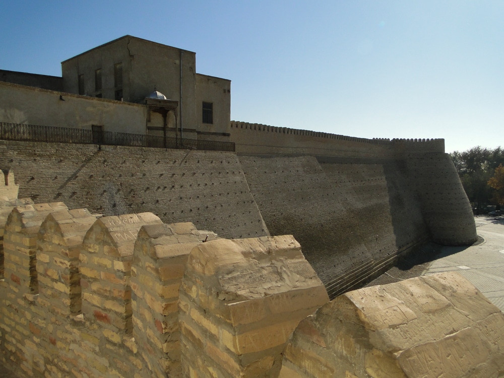 A fortress with massive slanting walls with crenellations on top of them.