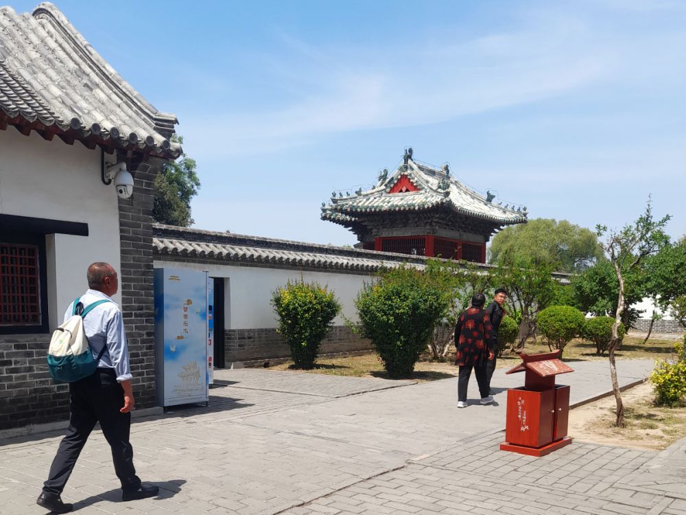 A few people walk along a wall, and a traditionally-roofed building is visible beyond the wall.