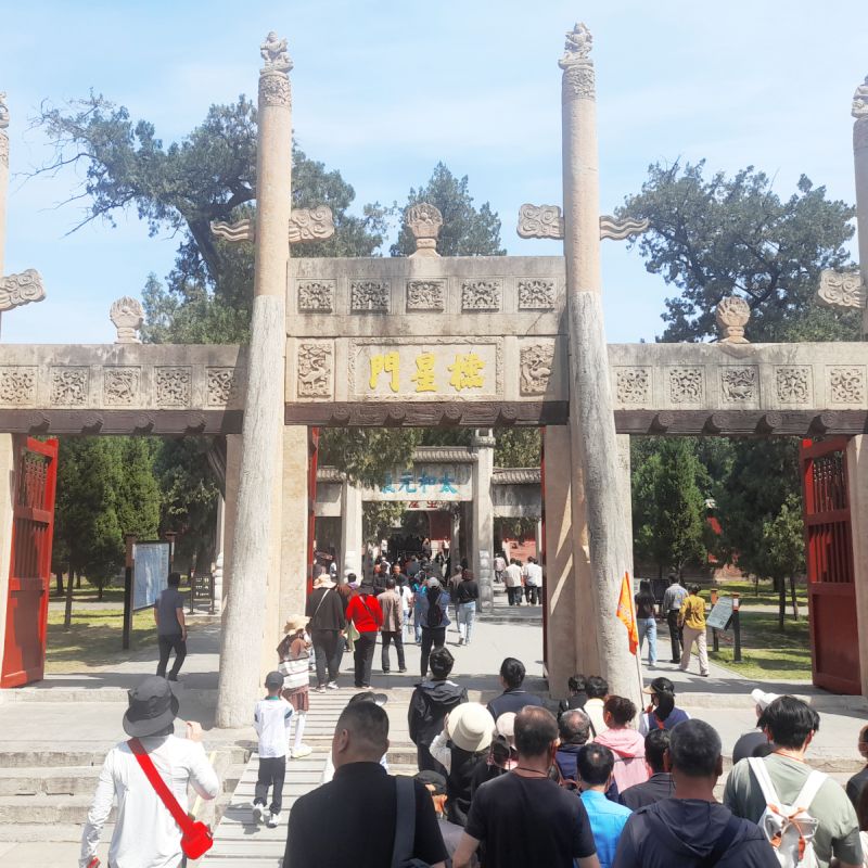 A large entrance gate engraved with calligraphy, and a group of people walking between the pillars.