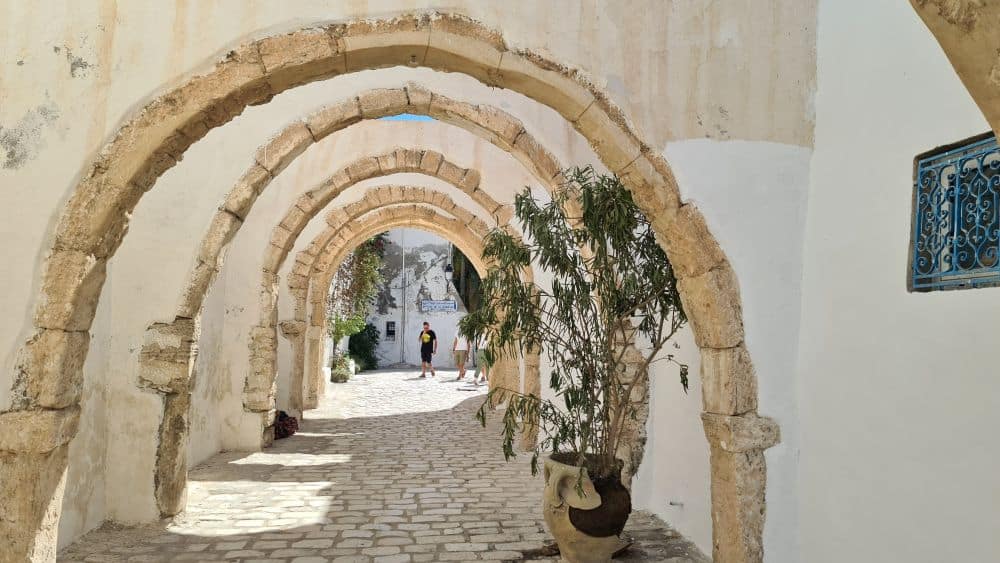 A series of stone arches cover a cobbled sidewalk in Djerba.