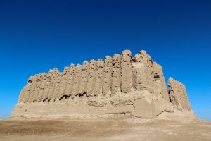 A large structure in stone with what looks like closely-set cylindrical columns around it.
