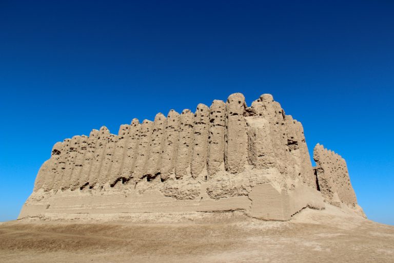 A large structure in stone with what looks like closely-set cylindrical columns around it.