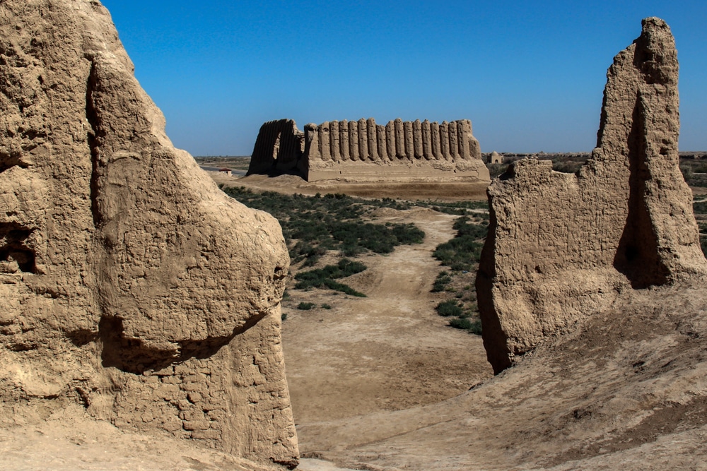 Looking down a path between ruins to a large stone structure in the distance.