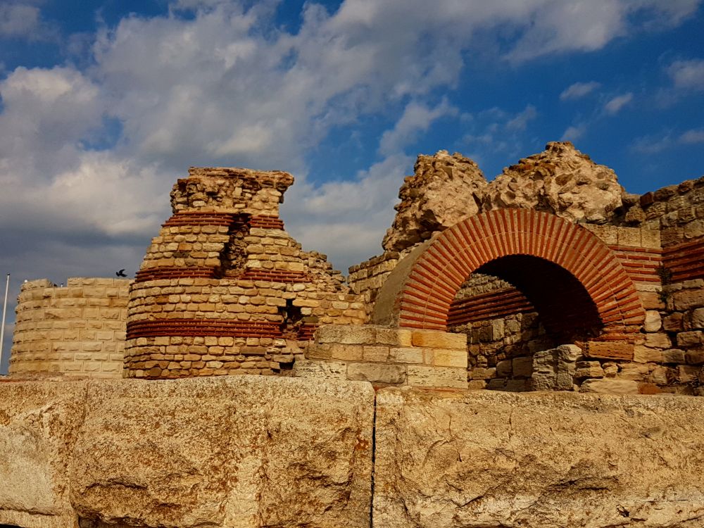 A brick arch and ruins of a brick wall with stripes of darker brick.