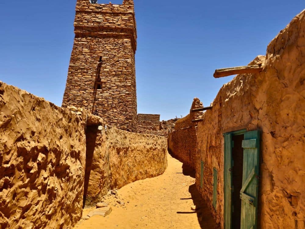 A narrow lane, stone walls on either side, and a tall square tower ahead.