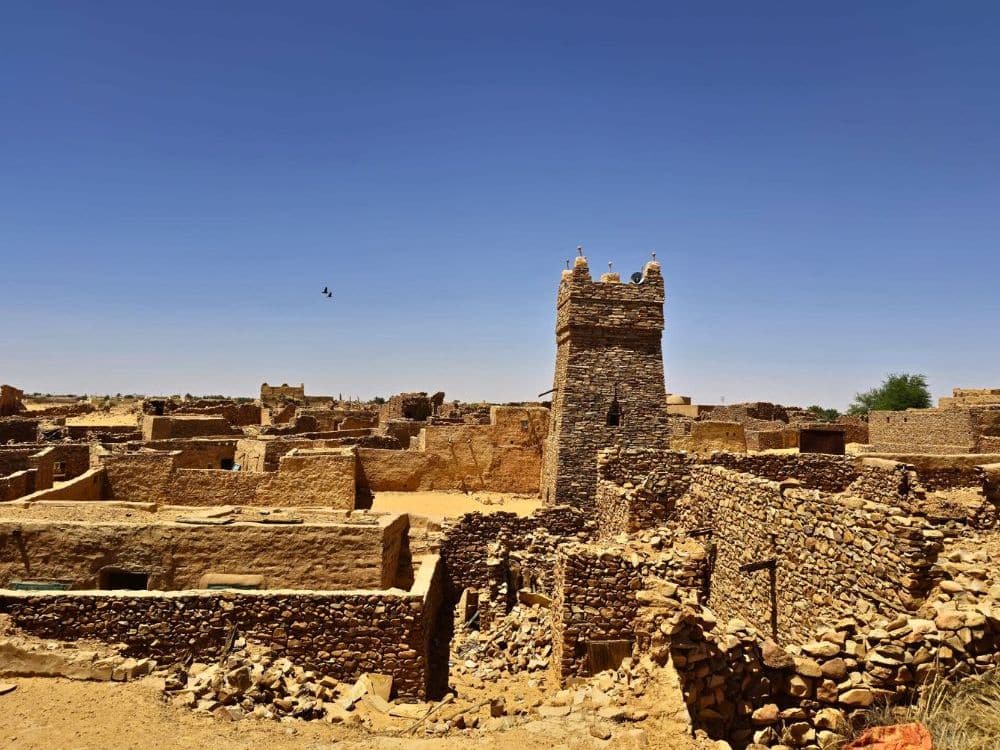 A view over a town of stone walls, with a small square tower in the middle.