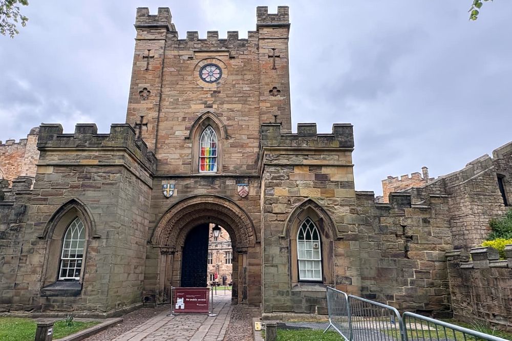 An archway in the stone castle, with a tower above the archway with crenellations on its roof.