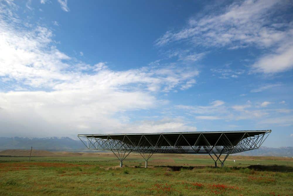 A large flat field with a large metal structure over an excavation site. Mountains on the horizon.